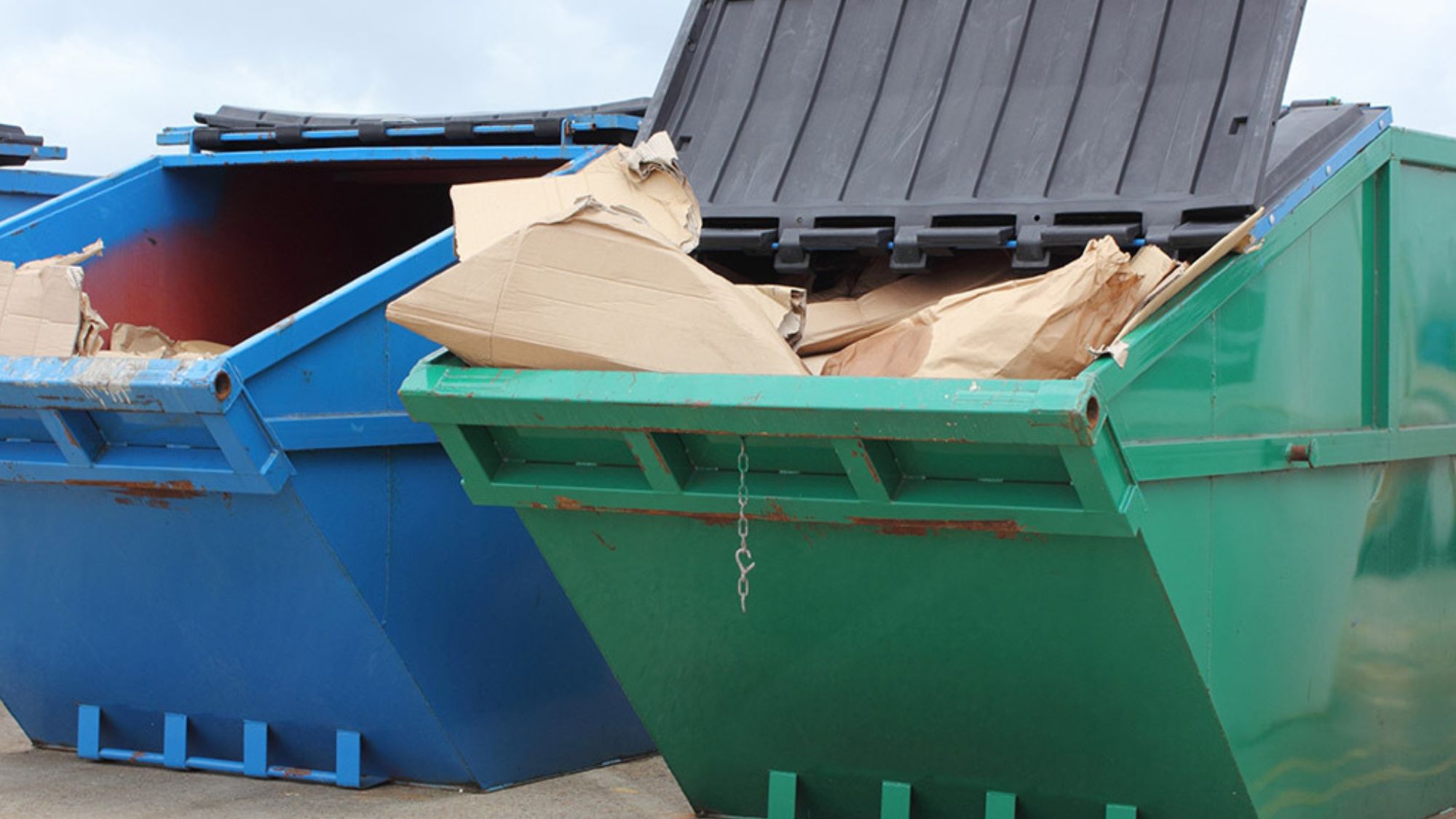 Two dumpsters in blue and green colors filled with cardboard boxes, representing a diverse range of options in skip hire service